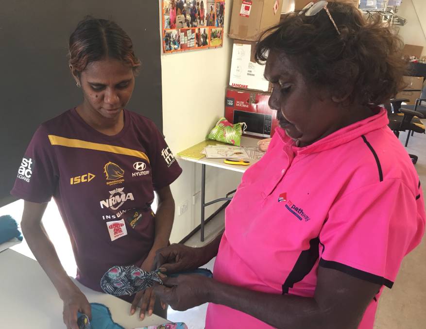 Two Indigenous Australian women work together indoors, focused on a hand-crafted project.
